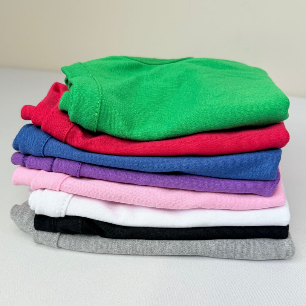 Stack of blank dog t-shirts in multiple colors including green, red, blue, purple, pink, white, black, and gray — wholesale pet apparel for customization
