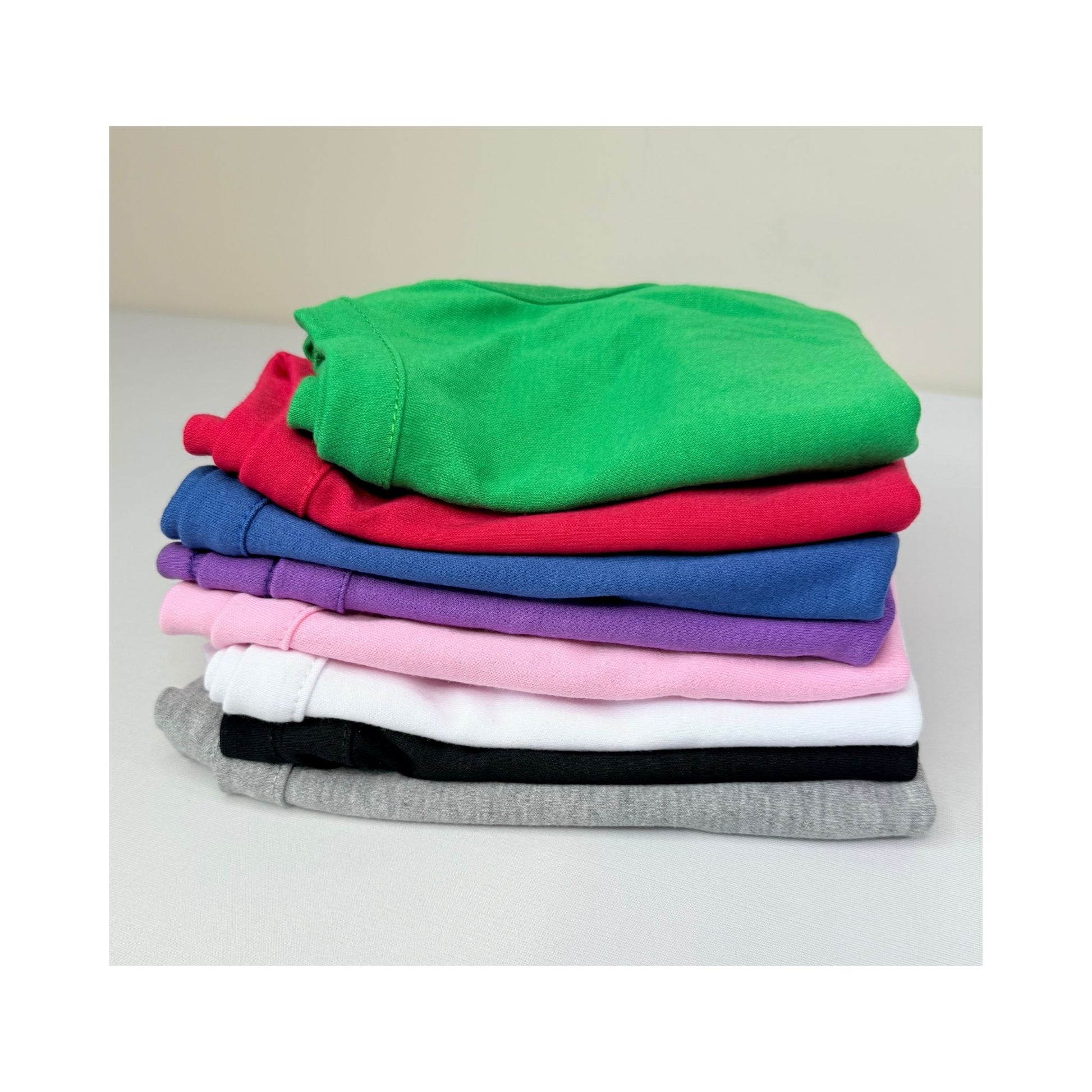 Stack of blank dog t-shirts in assorted colors - flat lay of pet apparel for small dog brands, crafters, and product photography